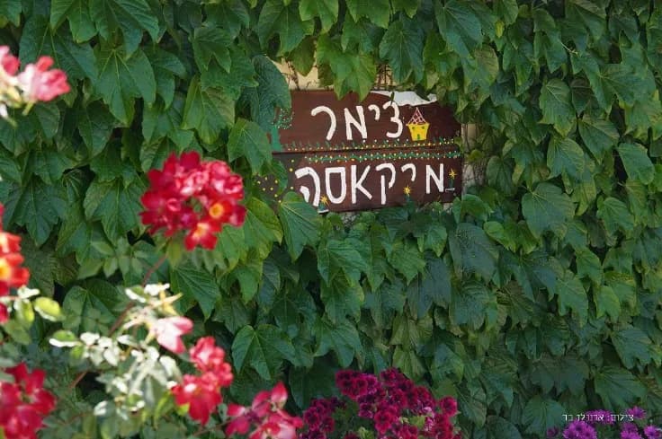 שלט צימר מיקאסה משובץ בקיר צמחייה ופרחים אדומים